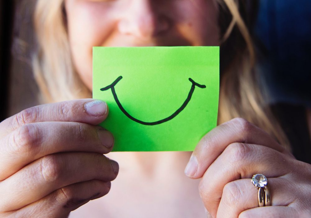 satisfacao-cliente-local-do-cidadao Pessoa a segurar um post-it com um sorriso desenhado, simbolizando satisfação e experiência positiva nos serviços do Local do Cidadão